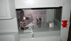 図２●5軸制御のデバリングセンターの加工室の切削工具（中央）とワークを取り付ける冶具（左）